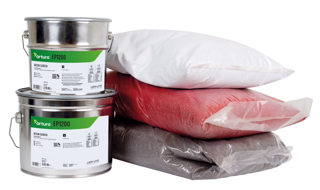 Arturo_Dummy_EP1200-74,25kg_2022-05 Studio photograph of two stacked metallic resin/paint cans labeled "arturo EP1200" with green labels, shown next to three sealed plastic bags of powdered pigments or aggregates in white, red and dark gray. The close-up image on a white background highlights metal handles, product labels and plastic packaging, suggesting materials for resin flooring or decorative screed.